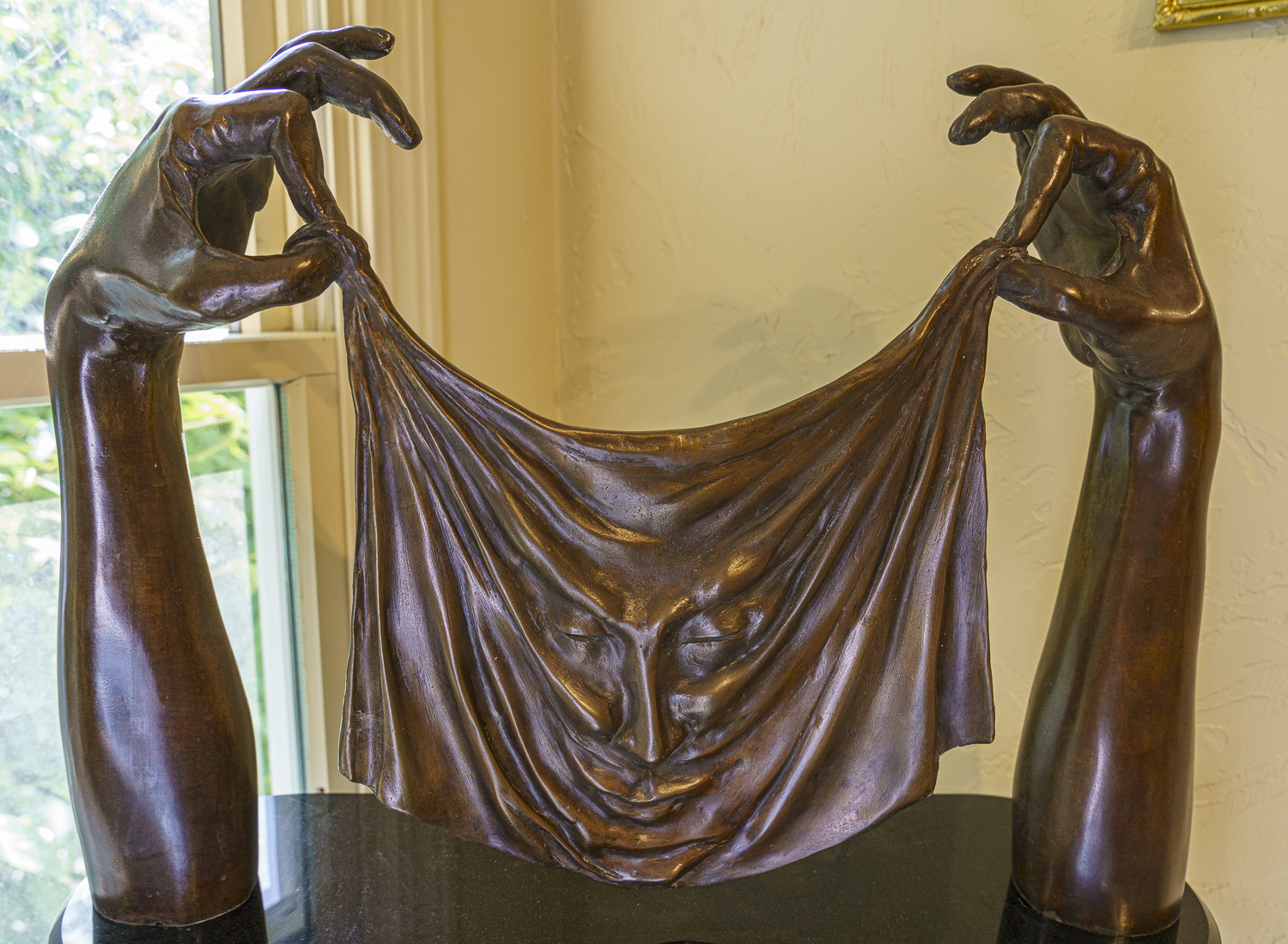 The sculpture called Abracadabra is shown as two arms holding a piece of fabric with a smiling face, all in bronze by artist Martin GLlck