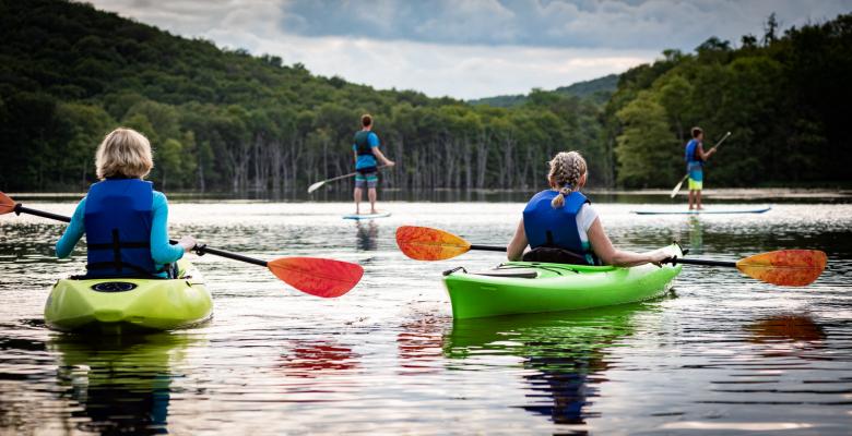 Two people kayaking on a lake in green boats with orange paddles